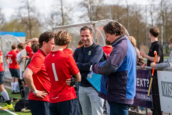 Een hockeyteam overlegt met de coach langs het veld
