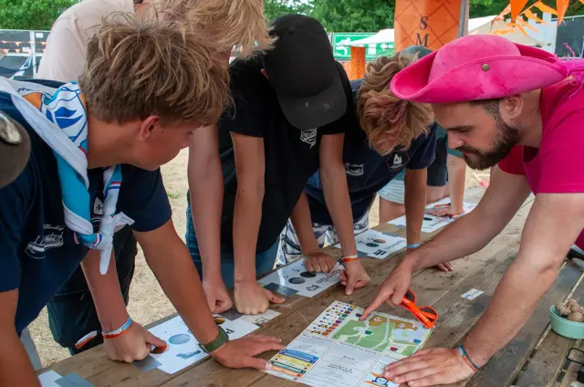 Een scoutingleider buigt met jongeren over een kaart